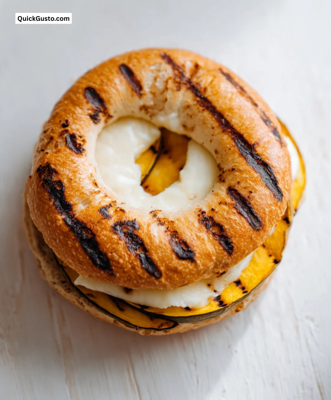 Grilled bagel topped with Swiss cheese and squash