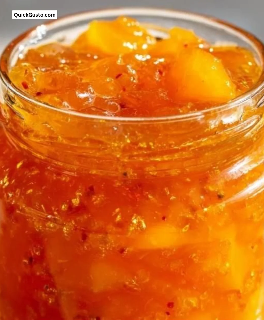 Homemade peach jam in a jar with fresh peaches and a wooden spoon.