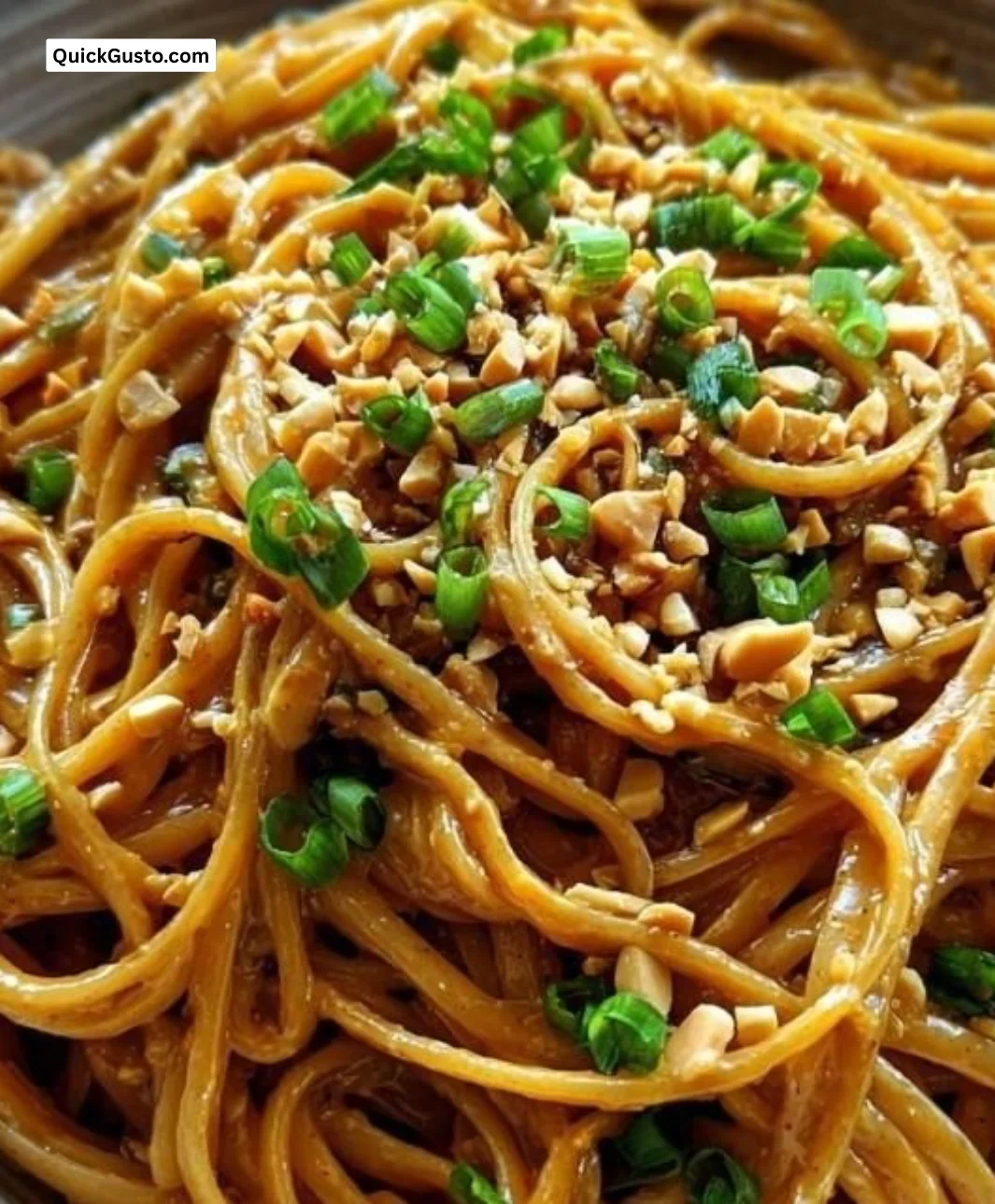 Bowl of sesame peanut noodles garnished with green onions and sesame seeds