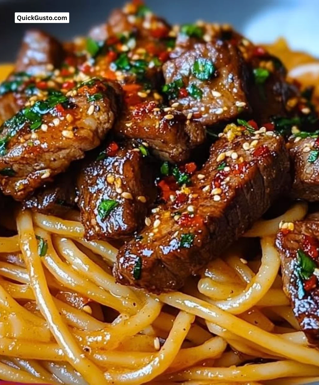 Delicious sweet and spicy garlic steak pasta on a plate, garnished with herbs.