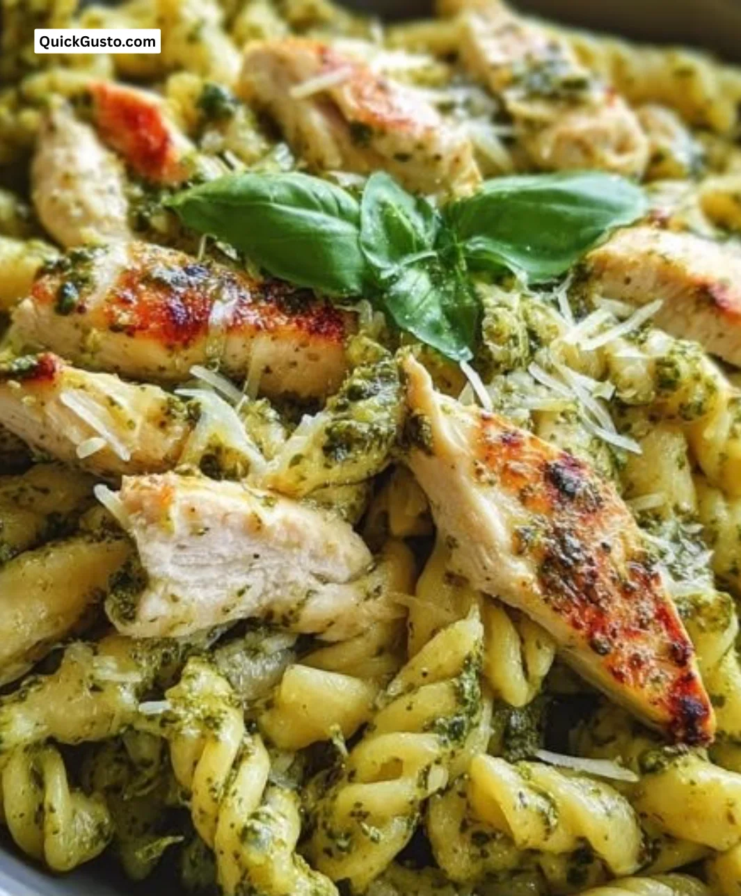 A bowl of Chicken Pesto Pasta topped with fresh basil and grilled chicken