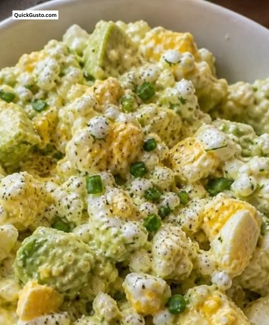 Creamy cottage cheese egg salad with avocado in a bowl, garnished with herbs.