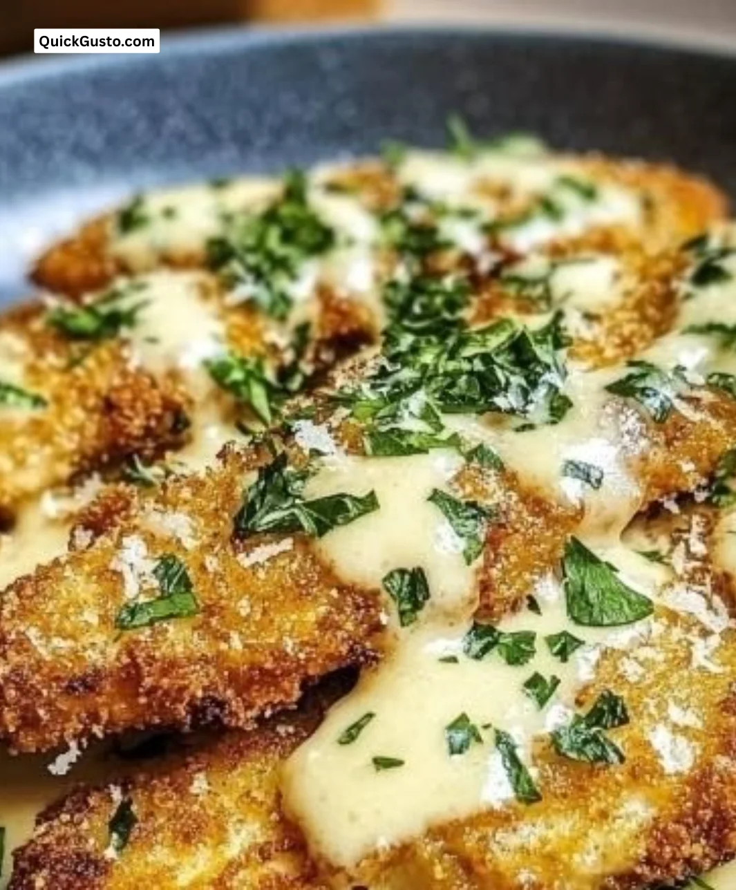 Crispy Parmesan chicken served with garlic cream sauce on a plate.