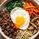 Bowl of easy bibimbap with vegetables, rice, and egg on a wooden table