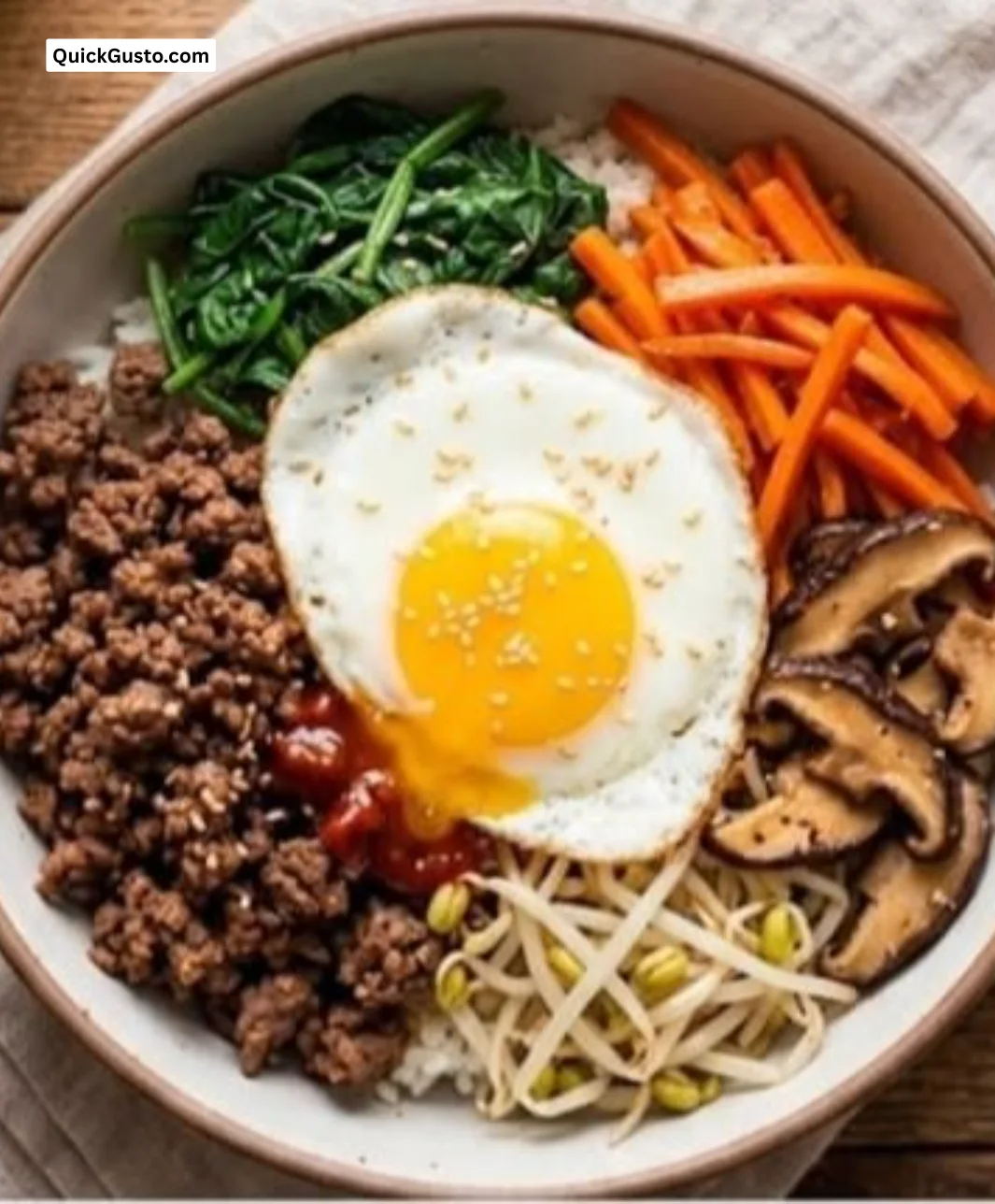 Bowl of easy bibimbap with vegetables, rice, and egg on a wooden table