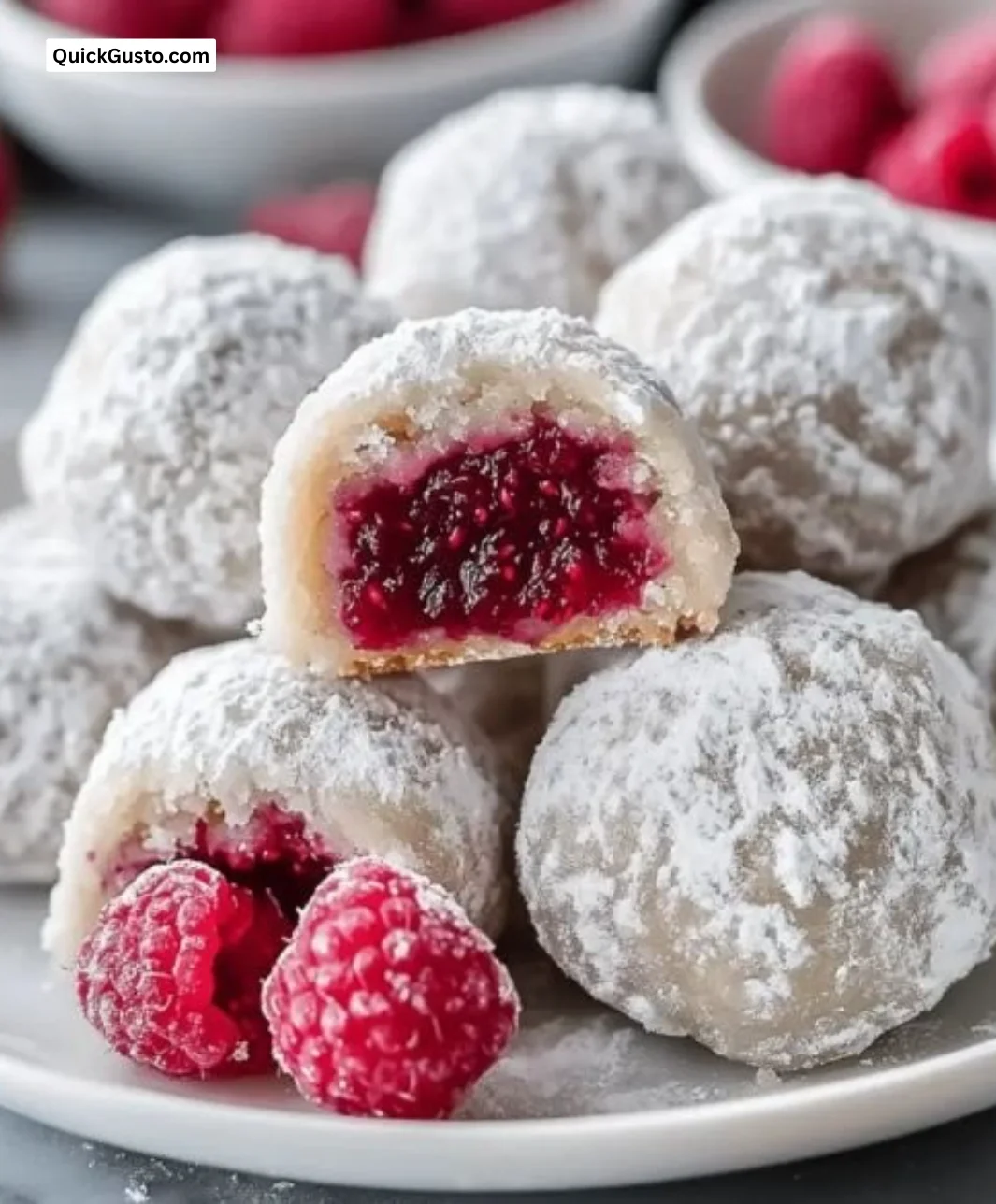 Raspberry-filled almond snowball cookies on a plate, dusted with powdered sugar