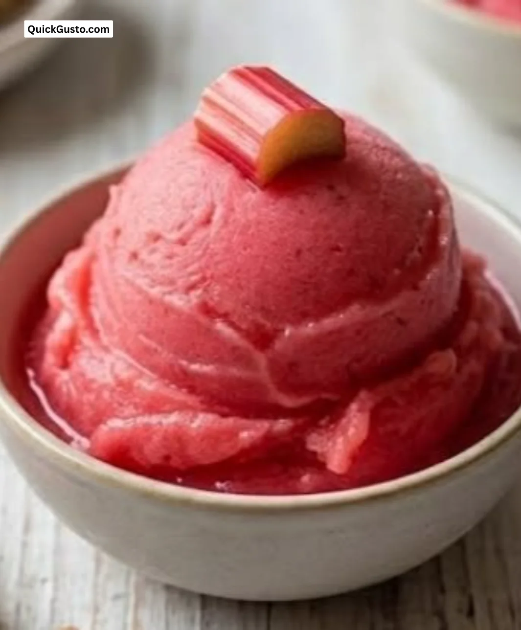 Homemade rhubarb sorbet in a bowl with fresh rhubarb stalks