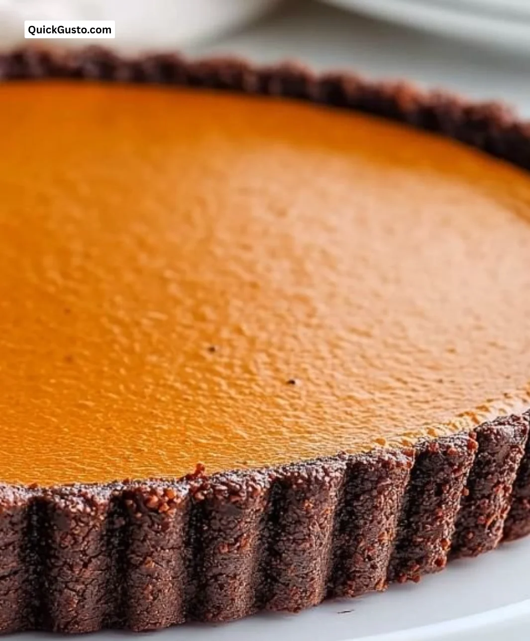 Silky dark chocolate pumpkin tart served with whipped cream in a cozy autumn setting