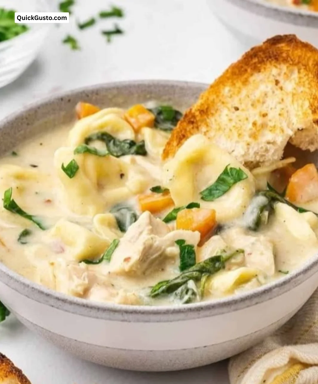 Bowl of creamy chicken tortellini soup garnished with herbs and vegetables